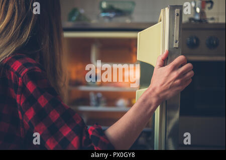 Eine junge Frau öffnet die Tür ihres Kühlschrank Stockfoto