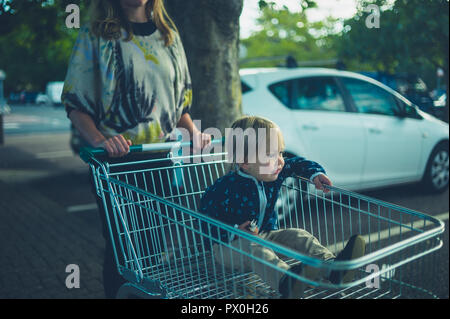 Ein kleines Kind wird, um in einem Einkaufswagen durch seine Mutter geschoben Stockfoto