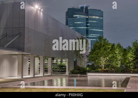 Der Garten auf dem Dach der Ginza 6 Shopping Mall in Tokio, Japan. Schuss in der Dämmerung, zeigt das Wasser mit Bäumen und einem nahe gelegenen Büro hochhaus. Stockfoto