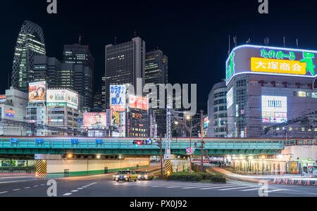 Ein Abend in der Nähe des geschäftigen Bahnhofs Shinjuku, Toyko, Japan, mit Leuchtreklamen, Büro- und Gebäuden, Werbetafeln, Eisenbahnen und Straßen. Stockfoto
