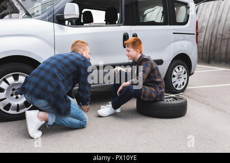 Vater anheben Auto mit Wagenheber für Reifenwechsel und Sohn Stockfoto