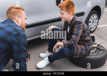 Vater und Sohn Reifenwechsel im Auto mit Wagenheber und bei jedem anderen Suchen Stockfoto