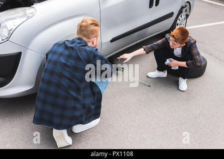 Vater mit dem Wagenheber anheben Auto für Reifenwechsel, Sohn zeigt auf etwas Stockfoto