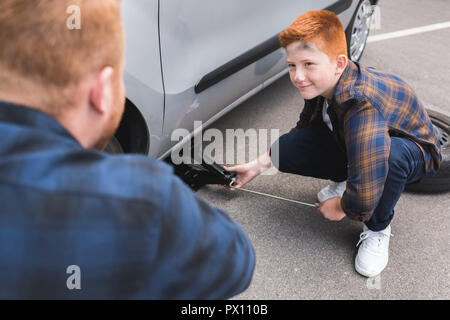 Sohn anheben Auto mit Wagenheber für Reifenwechsel und Vater Stockfoto