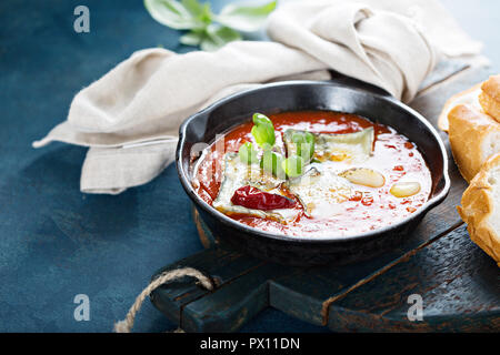 Gebratener Käse in Tomatensauce mit Knoblauch und Kräutern in einer gusseisernen Pfanne mit Baguette serviert. Stockfoto