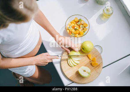 Ansicht von oben der schwangeren Frau mit Messer kochen Obstsalat zu Hause Stockfoto