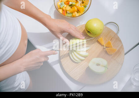 7/8 shot der schwangeren Frau mit Messer kochen Obstsalat zu Hause Stockfoto