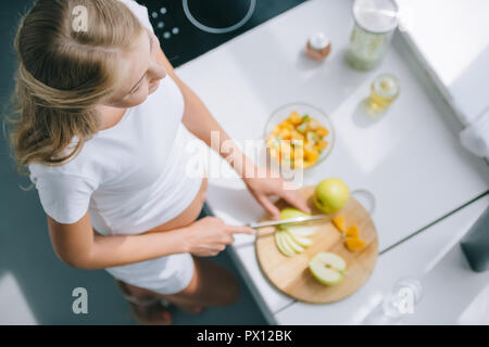 Ansicht von oben der schwangeren Frau mit Messer kochen Obstsalat zu Hause Stockfoto