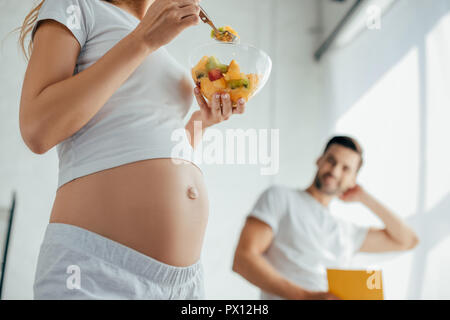 Teilweise mit Blick auf die schwangere Frau mit Obst und Salat Mann mit Buch in der Küche zu Hause. Stockfoto