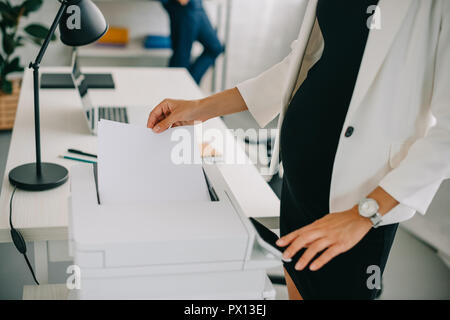 Teilansicht der schwangeren Unternehmerin mit Drucker im Büro Stockfoto