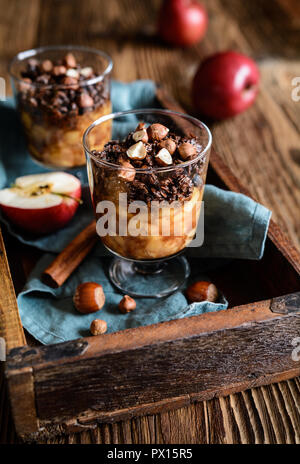 Gebackene Cinnamon Apple Stücke gekrönt mit Schokolade Müsli und Haselnüsse in Gläsern Stockfoto