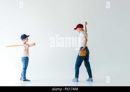 Seitenansicht von Mutter Pitching baseball ball Sohn mit Baseballschläger isoliert auf weißem Stockfoto