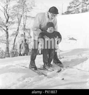 Winter in den 60er Jahren. Ein Vater und sein Sohn sind, genießen Sie einen Tag im Winter Skifahren. Der Junge bekommt einige sich auf den Skiern zu balancieren. Es ist ein Tag der Winter Sport an Fiskartorpet in Stockholm, Februar 1960. Stockfoto