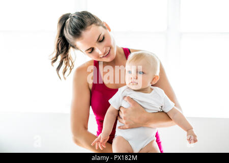 Ein Porträt der schöne junge Mutter in Sportbekleidung mit ihren charmanten kleinen Baby im Training Stockfoto