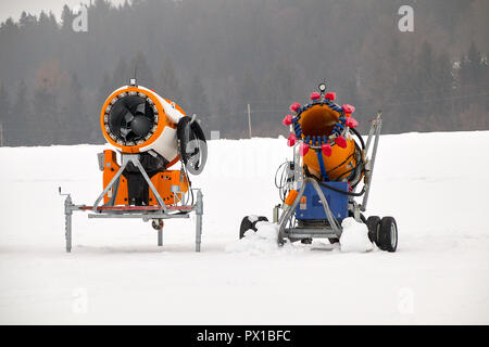 Zwei verschiedene Schneekanonen stehen im Schnee und warten auf ihre Mission in Tirol, Österreich. Stockfoto