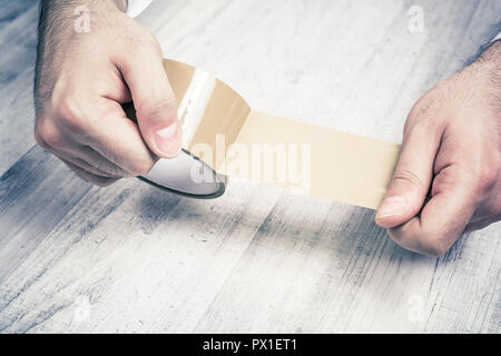 Männliche Hände halten ein Abgerollt Packband über Holz- Tabelle Stockfoto
