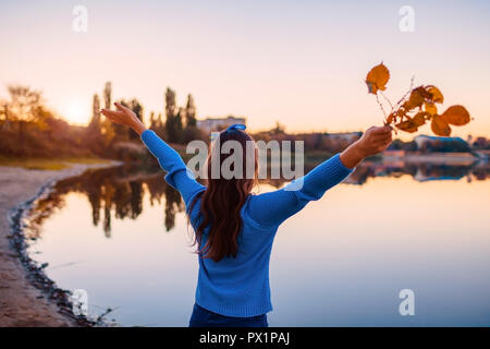 Junge Frau bewundern Herbst Fluss Szene mit angehoben und geöffnete Hände halten Branchen. Release und freie Energie Stockfoto