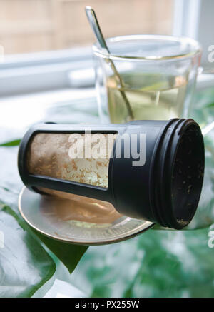 Im Vordergrund steht der Tee Filter, dann haben wir das transparente Glas Schale mit hellen Kaffee und die Löffel. Stockfoto