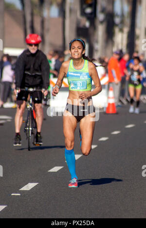 Ein Hispanic Halbmarathon weibliche Sieger nähert sich die Ziellinie auf einer Straße in Huntington Beach, CA. Hinweis Fahrrad Escort. Stockfoto