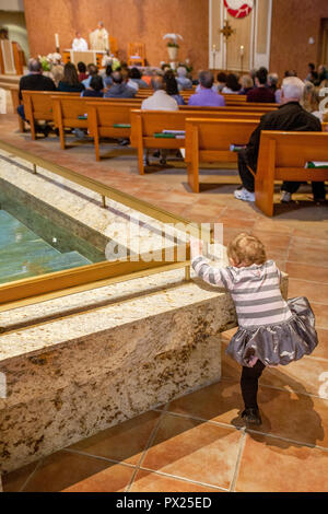 Ein Kleinkind Mädchen versucht, Klettern in das Taufbecken während der Messe an einer katholischen Kirche in Laguna Niguel CA. Stockfoto