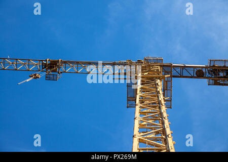 Gelbe metall Kran vor einem Gebäude in einer Baustelle von unten an einem sonnigen Nachmittag montiert wird, unter einem blauen Himmel Bild Stockfoto