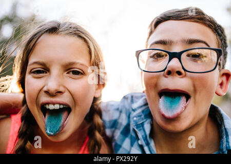 Happy Teenager Jungen und Mädchen Spaß im Freien. Aufgeregt, Jungen und Mädchen mit ihren bunten Zunge nach dem Verzehr von Süßigkeiten. Stockfoto