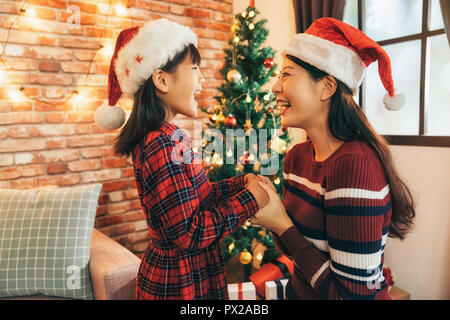 Schöne Mama an der Hand santa girl Kid und Lächeln freudig. schöne Tochter und Mutter in Santa hat zu Hause. Frohe Weihnachten und schöne Feiertage! Stockfoto