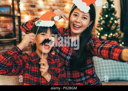 Junge Frau und schöne Tochter mit schwarzen Schnurrbart Spaß zu Hause am Heiligabend. Santa Mädchen unter Geschenk Boxen in der Nähe von Weihnachten Baum. Familie Cele Stockfoto