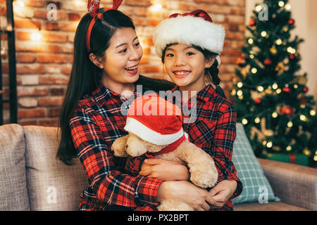 Schöne junge Mutter umarmt Tochter mit Liebe an Heiligabend. schöne Familie sitzt im Wohnzimmer in Weihnachten Urlaub. Die Familie Weihnachten feiern e Stockfoto