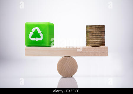 Grün Cubic Block mit Papierkorb Symbol und goldenen Münzen Balancing auf Holz- Wippe Stockfoto