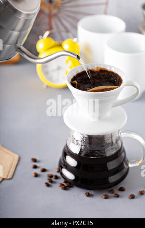 Über Kaffee mit einem Wasserkocher und Glas Karaffe mit heißem Wasser gegossen werden und Wecker im Hintergrund, Gießen Stockfoto