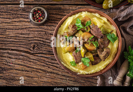 Gebratenes Huhn Leber mit Äpfel, Paprika und Zwiebeln mit Kartoffelpüree als Close-up in einer Schüssel auf Holztisch. Ansicht von oben. Flach. Stockfoto