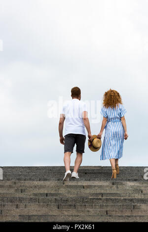 Ansicht der Rückseite des Paar hält Strohhut und wandern auf der Treppe gegen bewölkter Himmel Stockfoto