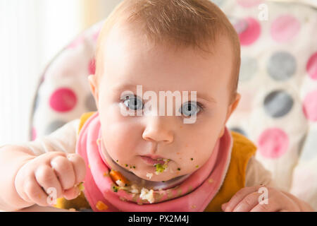 Ein weißes Baby mit blauen Augen abgebildet mit Essen über sein Gesicht, als er beginnt baby Abstillen geführt. Stockfoto