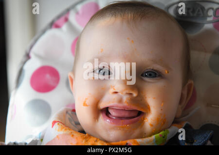 Ein weißes Baby mit blauen Augen abgebildet mit Essen über sein Gesicht, als er beginnt baby Abstillen geführt. Stockfoto
