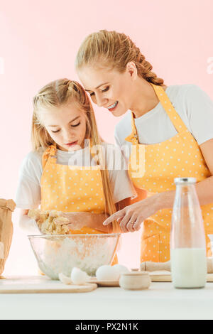 Glückliche Mutter lehre Tochter wie Teig isoliert auf Rosa zu kneten Stockfoto