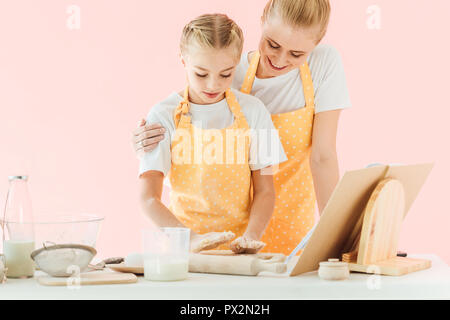 Glückliche junge Mutter und Tochter gemeinsam isolierte Kochen auf Rosa Stockfoto