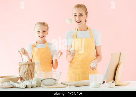 Glückliche Mutter und Tochter jonglieren mit teiglinge beim Kochen auf rosa isoliert Stockfoto