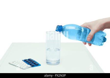 Die Hand des Mädchens gießt Wasser aus der Flasche in das Glas. In der Nähe liegen der Verpackung mit Tabletten. Stockfoto