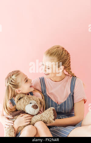 Mutter und Tochter mit Teddybär umarmen und an jedem anderen Suchen isoliert auf Rosa Stockfoto