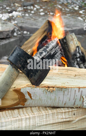 Ax und Brennstämme vor einem im Freien Feuer vertikal Stockfoto