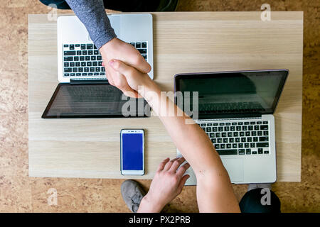 Zwei junge Menschen, die auf den Laptops im Büro. Am Tisch sitzen einander gegenüber, Handshake, Ansicht von oben, close-up Stockfoto