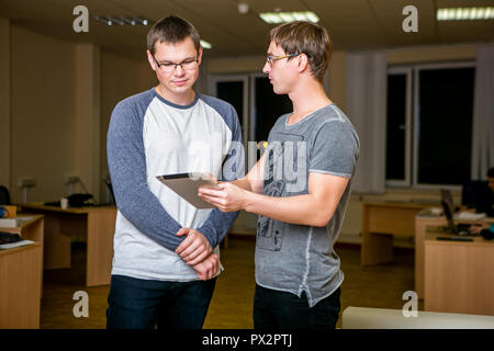 Zwei junge Menschen diskutieren über ein Projekt im Büro. Neben einander, eine von ihnen erzählt den anderen über sein Projekt und zeigt auf die Tafel, eine Diskussion führen. Stockfoto