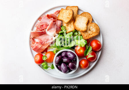 Antipasti Teller mit getrockneten Brot, Schinken Serrano, Tomate Kirsche und violette Oliven. Weißer Hintergrund Stockfoto
