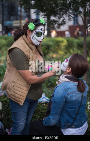 Eine make-up-artist, tragen typische "catrina" Make-up, setzt auf Make-up einer jungen Frau am traditionellen Tag der Toten Parade in Mexiko Stadt Stockfoto