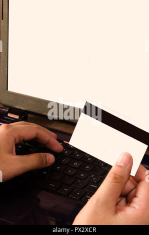 Kreditkarte durch einen Mann gehalten, mit Blick auf die Kamera rechts unten, Hände einen Mann auf einem Laptop Computer Einkäufe online. Stockfoto