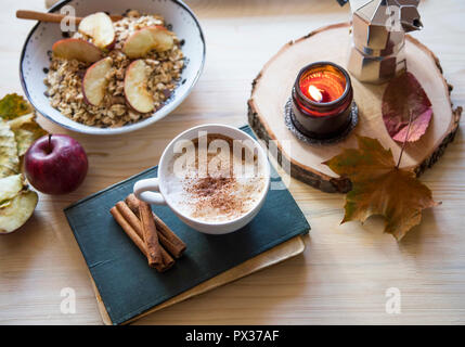 Herbst am Morgen Kaffee Cappuccino Tasse mit Zimt, duftende Kerze, Apple Müsli Schüssel, Buch, Herbst Inneneinrichtung Zusammensetzung Stockfoto