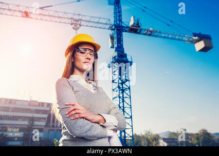 Schöne Frau Bauingenieur lächelnd mit Zuversicht vor einem Kran in einem Sonnenuntergang flare Hintergrund Stockfoto