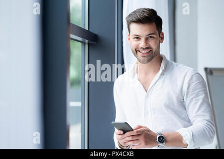 Ein junger Mann Geschäftsmann vor der Kamera, während Sie ein Smartphone. Über Geschäft, Erfolg kommunizieren, junges Unternehmertum, Startups, Finanzen Stockfoto