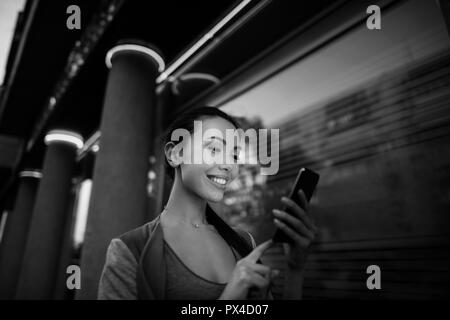 Schwarz-weiß Bild von einer asiatischen Frau mit einer Anwendung in Ihrem smart phone E-Mail zu lesen, SMS senden, Chat, Surfen oder online einkaufen Stockfoto